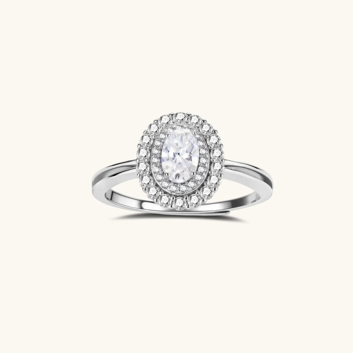 Sterling silver ring with oval moissanite center stone surrounded by double halo of sparkling stones on neutral background.