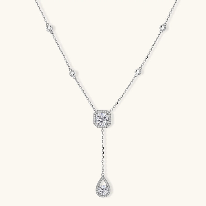 Sterling silver necklace with cushion-cut moissanite in halo setting and teardrop pendant, displayed on cream background.