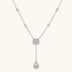 Sterling silver necklace with cushion-cut moissanite in halo setting and teardrop pendant, displayed on cream background.