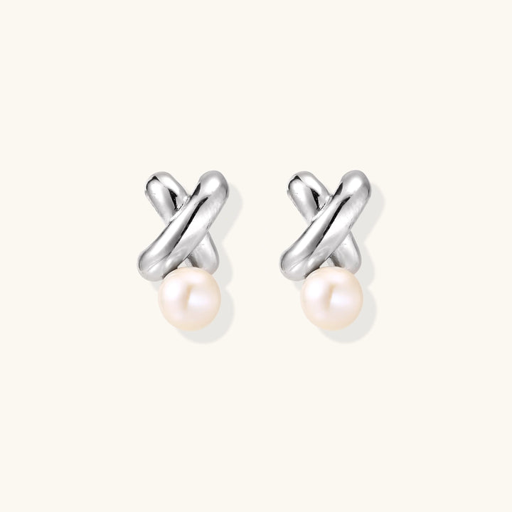 Rhodium-plated silver earrings with twisted X design and freshwater pearl drops on beige background