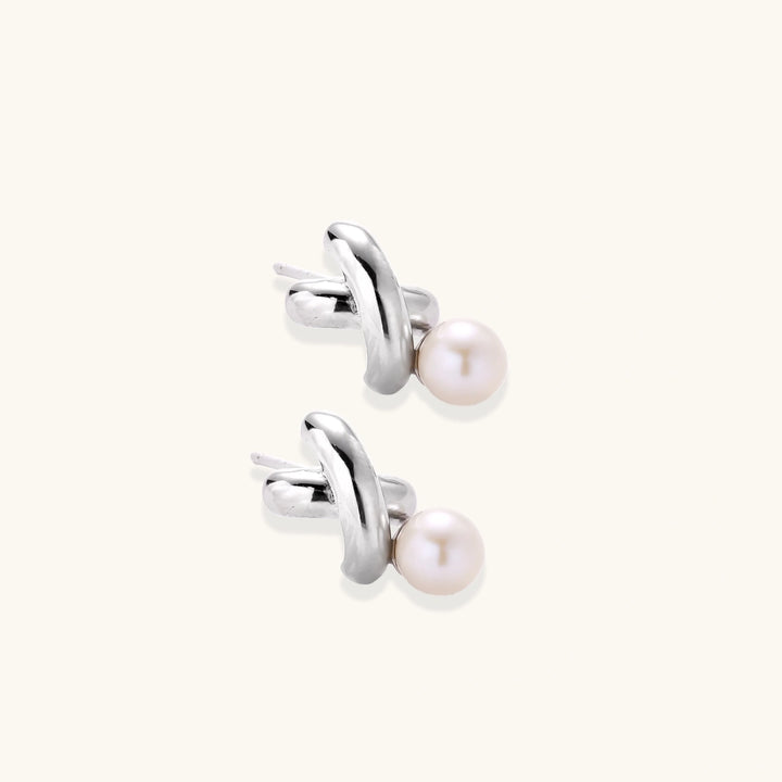 Rhodium-plated silver earrings with twisted X design and freshwater pearl drops on beige background
