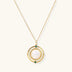 Gold pendant necklace with circular orbital design, iridescent mother-of-pearl center, and green zirconia accents