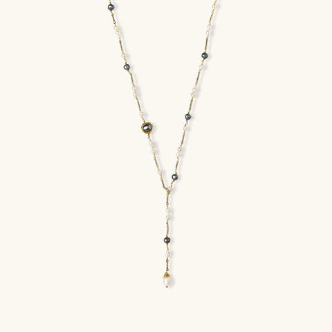 Y-shaped gold-plated necklace with white and gray freshwater pearls on cream background, showing adjustable drop design.