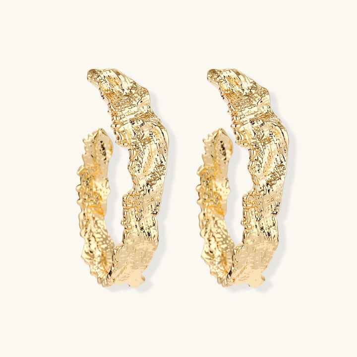 Close-up of sculptural hoop earrings with organic molten texture in silver and gold finishes on white background