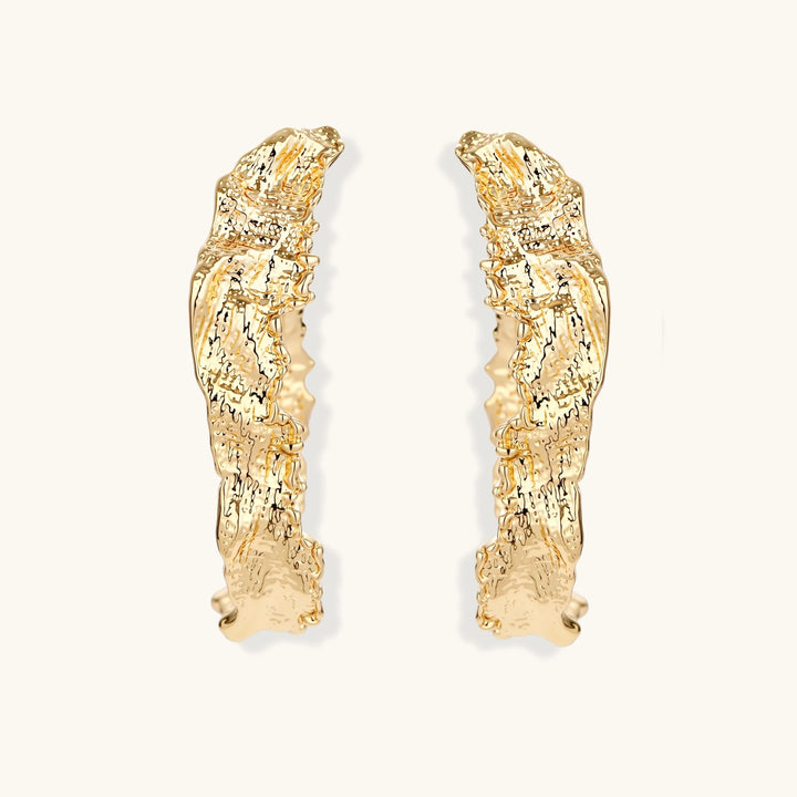 Close-up of sculptural hoop earrings with organic molten texture in silver and gold finishes on white background
