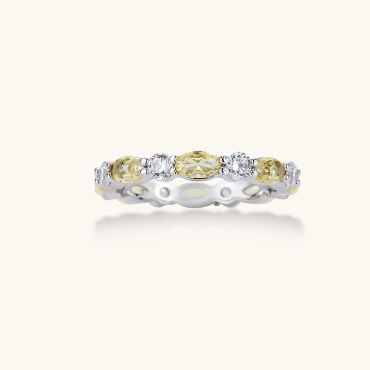 Platinum-plated copper ring with alternating clear and pale yellow oval stones in an eternity band design on white background.